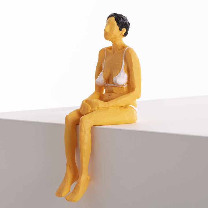 Seletti Love Is a Verb Penelope Figurine, ochre resin woman in a white bikini sitting on a ledge, hands in her lap