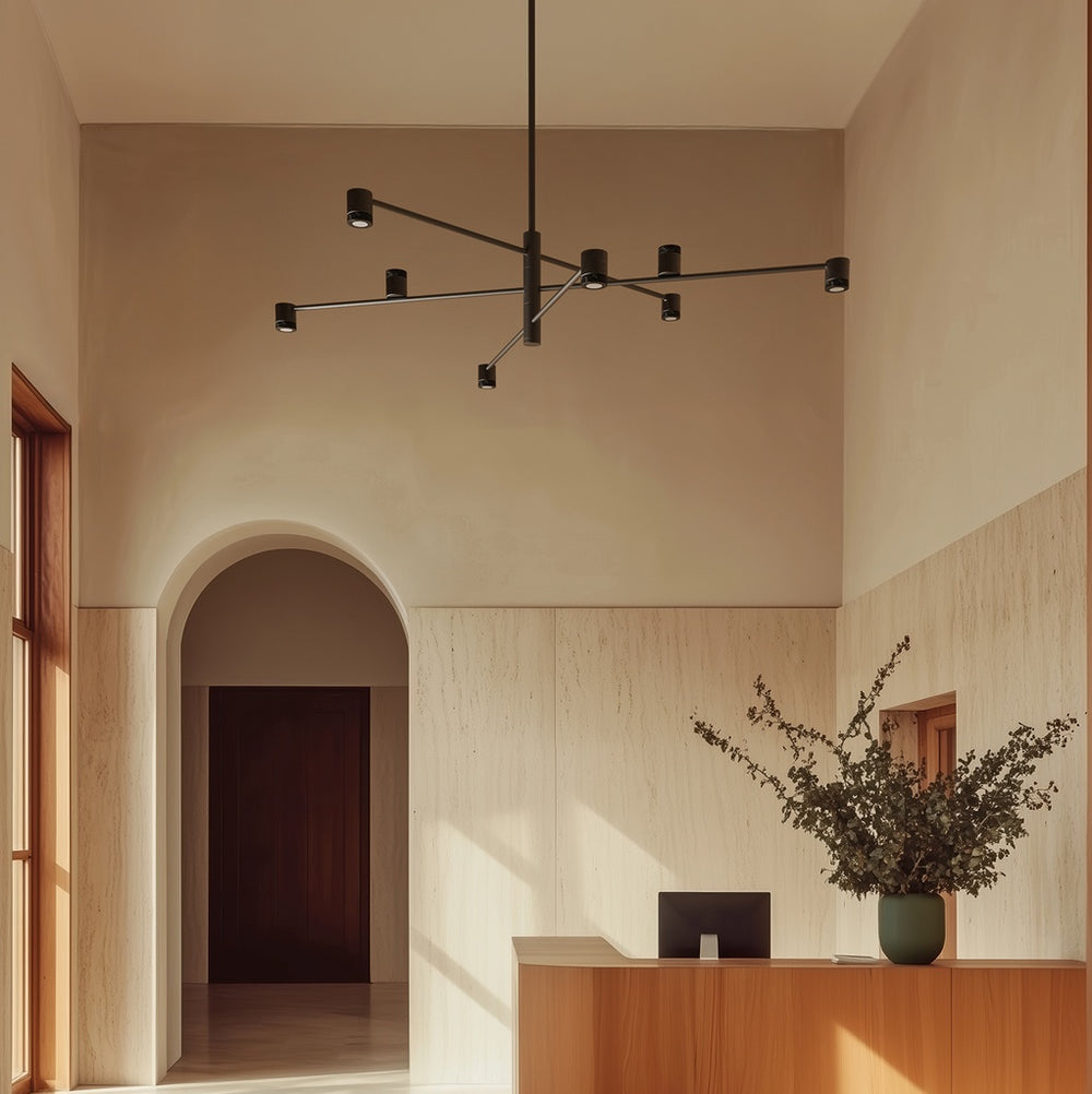Tea Chandelier in matt black hanging in a tall travertine lobby above a wooden reception desk