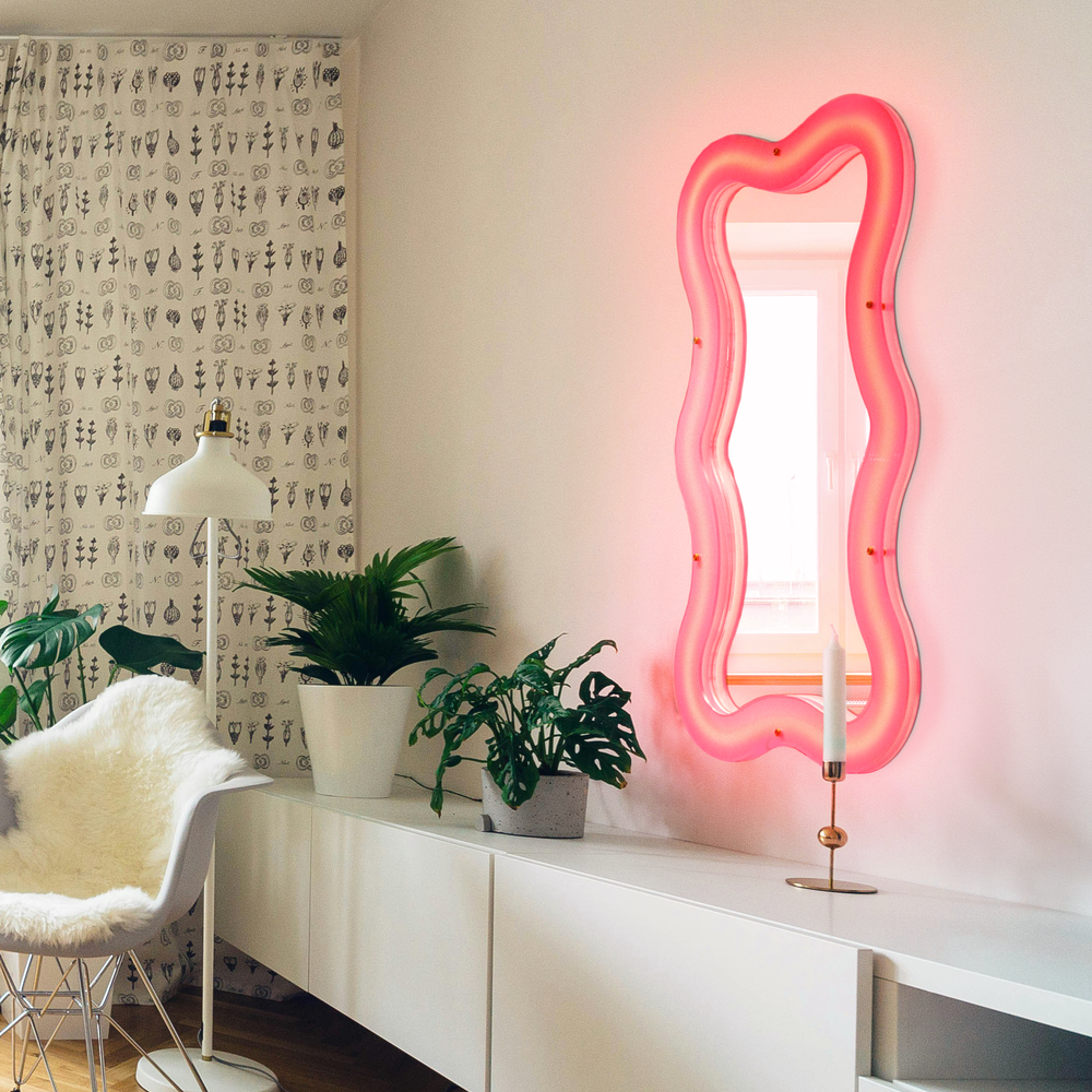 Seletti Supercurve Wavy Mirror Tiny Tall, the mirror glowing pink above a white sideboard with plants
