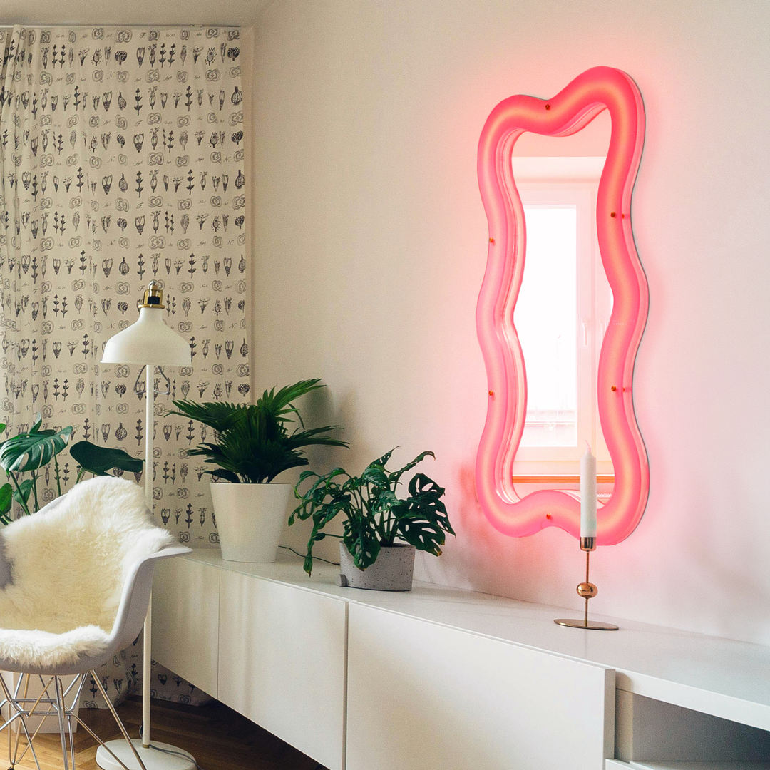 Seletti Supercurve Wavy Mirror Tiny Tall, the mirror glowing pink above a white sideboard with plants