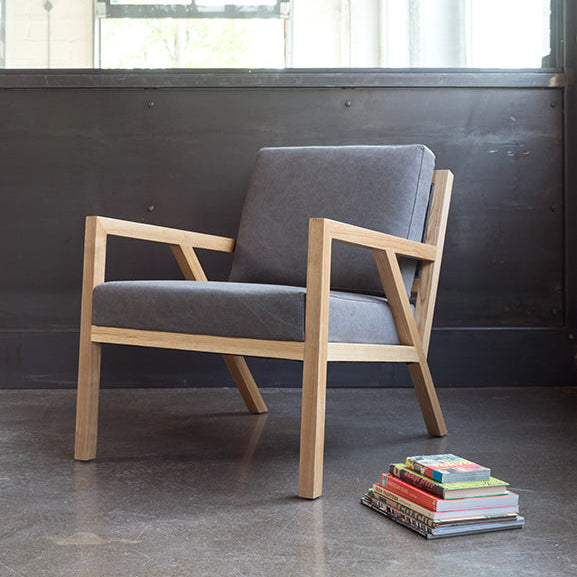Modern oak armchair with gray upholstery, styled beside colorful books in an industrial loft