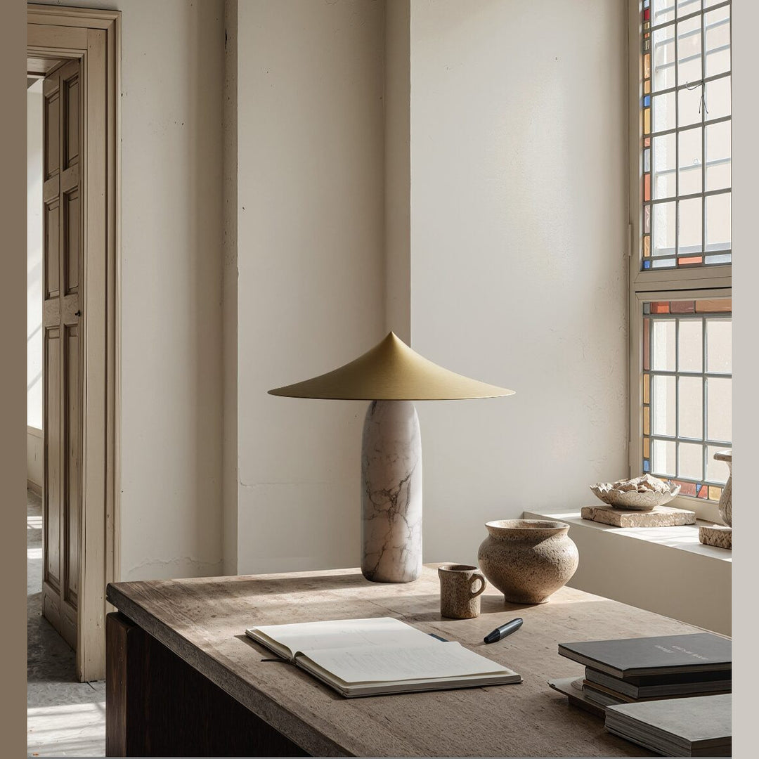 Kine Table Lamp with brass conical shade and veined marble body on a rustic wooden desk by a stained-glass window