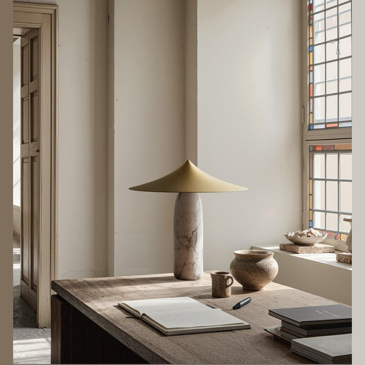 Kine Table Lamp with brass conical shade and veined marble body on a rustic wooden desk by a stained-glass window
