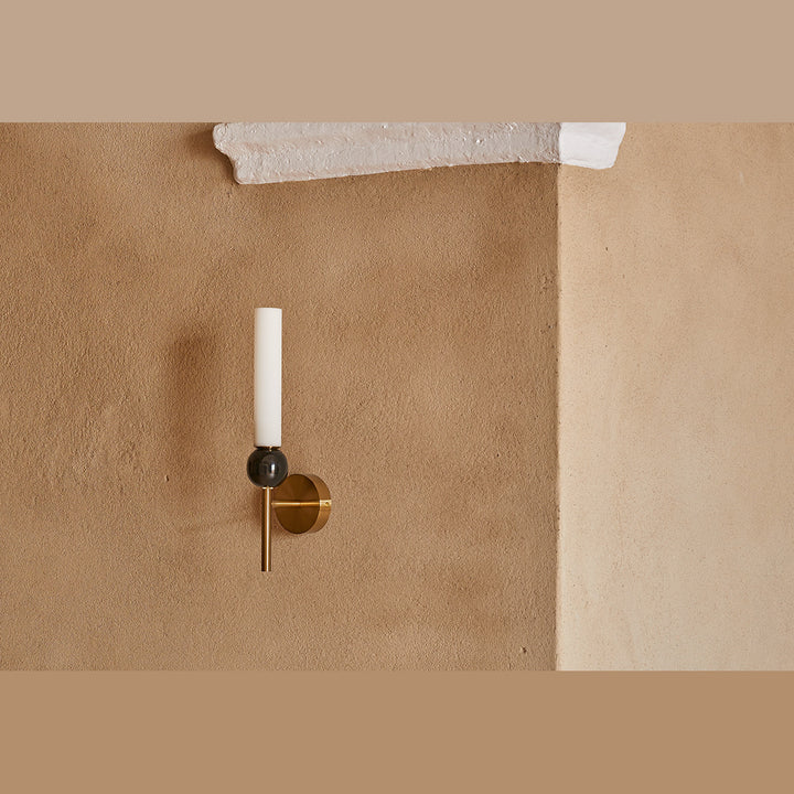 Aged gold Delie Wall Lamp with black marble sphere and opal tube shade on a warm ochre plaster wall