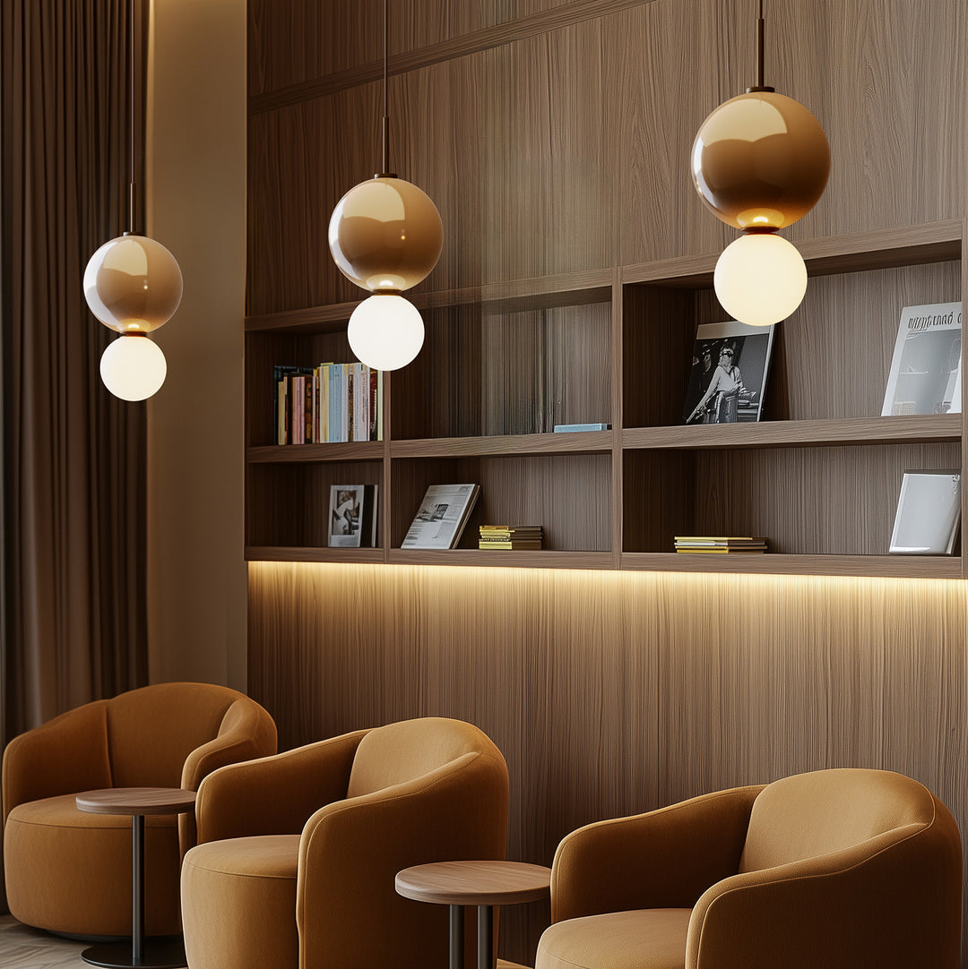 Ulon Pendant Lamp trio lit at staggered heights above amber lounge chairs and walnut shelving