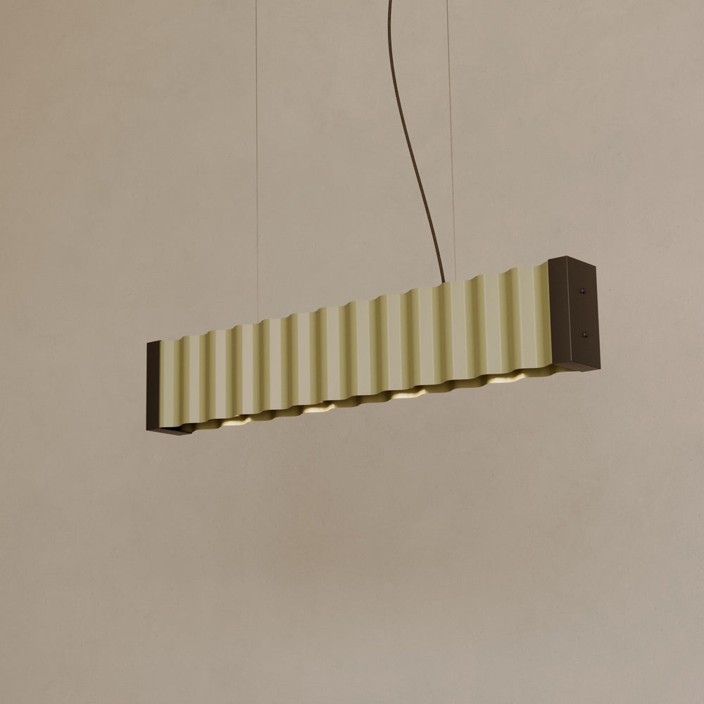 Nosa Pendant Lamp with pale green corrugated panels and dark bronze end caps, hung on fine cables against a warm wall