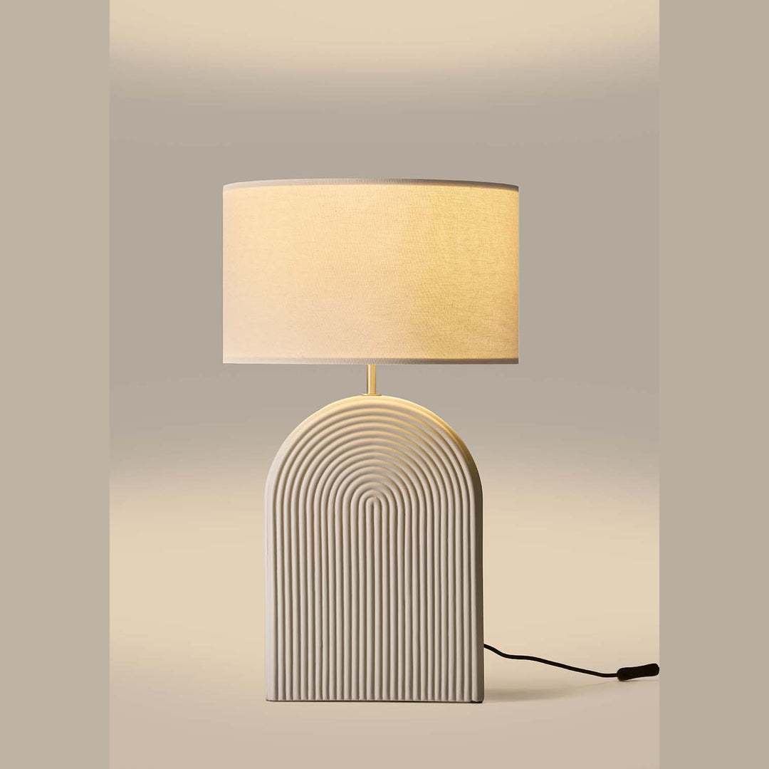Lopo Table Lamp with cream arched ceramic base in concentric grooves and linen drum shade, lit