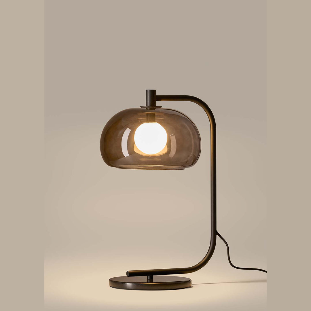 Cloud Table Lamp lit in profile, smoked glass dome over a globe bulb on a dark curved arm and disc base