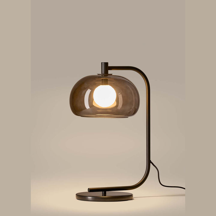 Cloud Table Lamp lit in profile, smoked glass dome over a globe bulb on a dark curved arm and disc base