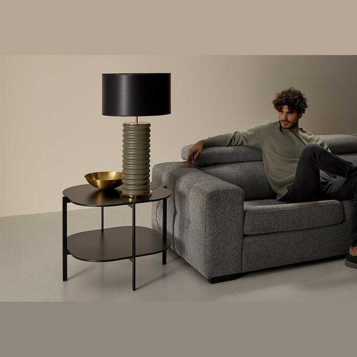 Taro Table Lamp with olive green ribbed base and black drum shade on a black side table beside a grey sofa