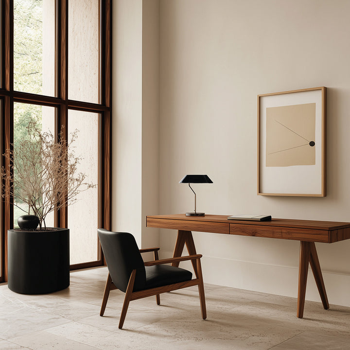 Aider Table Lamp with black shade on a wooden desk beside a black leather lounge chair and tall windows