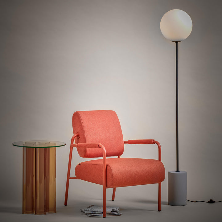 Orange armchair with a small round table and floor lamp against a gray wall.