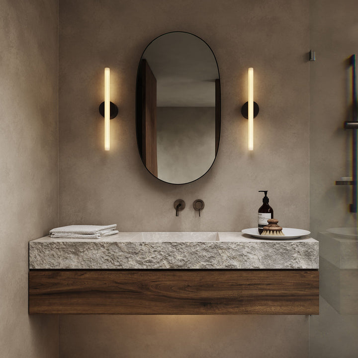 Modern bathroom vanity with stone countertop, wood base, oval mirror, and vertical sconces