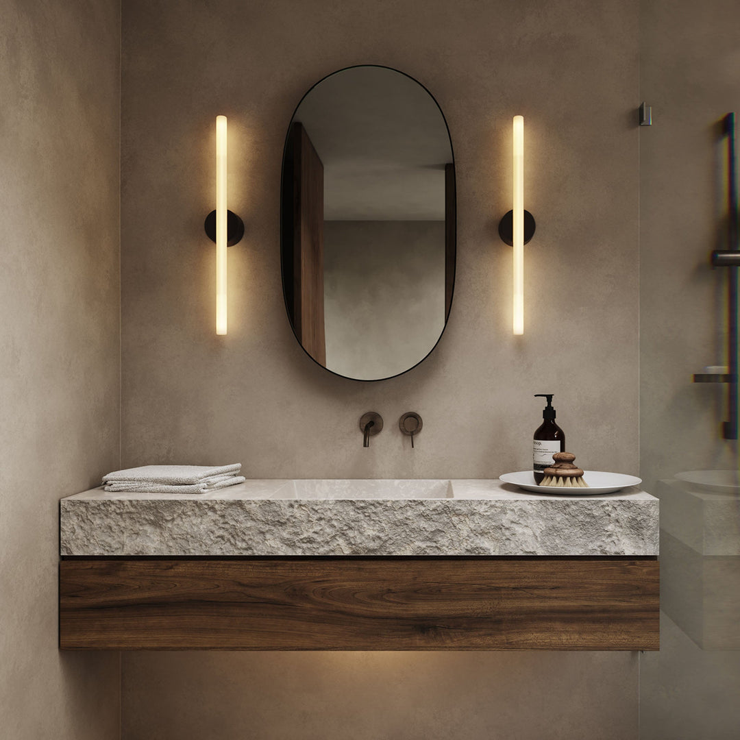 Textured stone vanity with walnut base, oval mirror, and sleek wall sconces