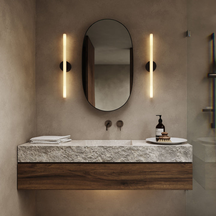 Textured stone vanity with walnut base, oval mirror, and sleek wall sconces