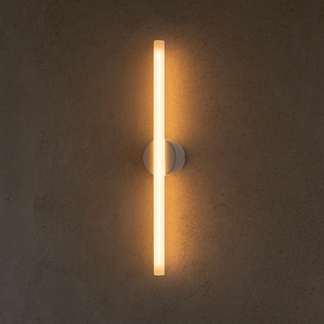 Modern LED wall sconce with minimalist design, emitting warm ambient glow against textured concrete wall