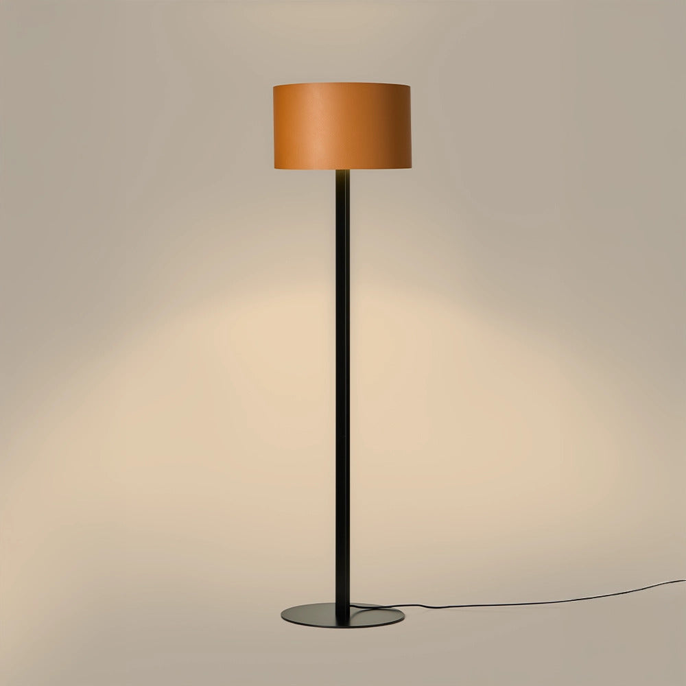 Rems Floor Lamp lit, orange leather shade casting a warm glow down a beige wall