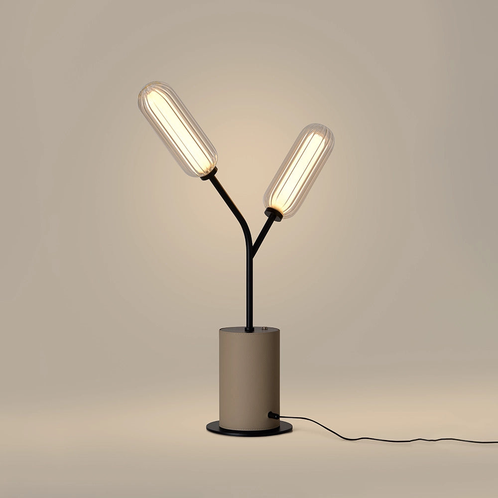 Lari Table Lamp switched on, two ribbed glass shades glowing warm above a taupe leather base