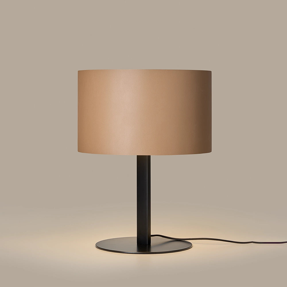 Tan leather shade lamp lit, casting a warm glow onto its black disc base