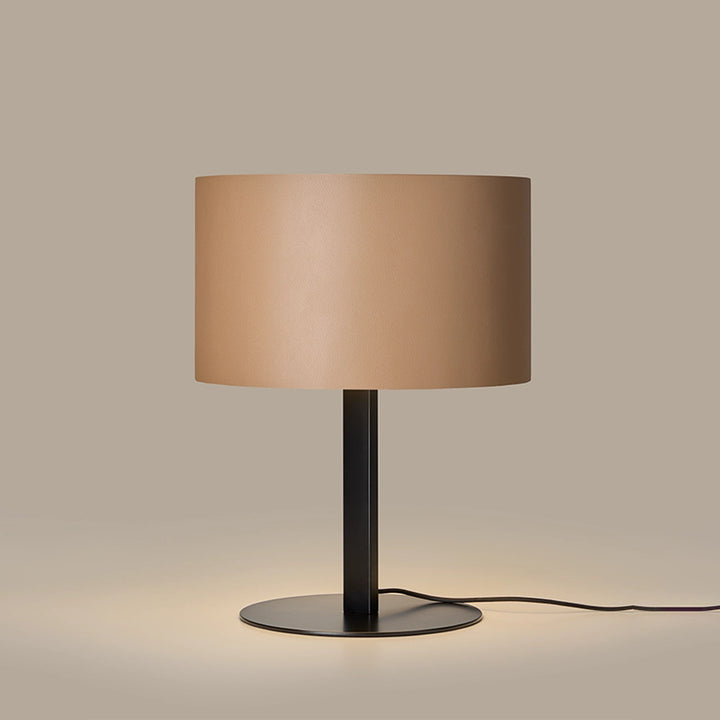 Tan leather shade lamp lit, casting a warm glow onto its black disc base