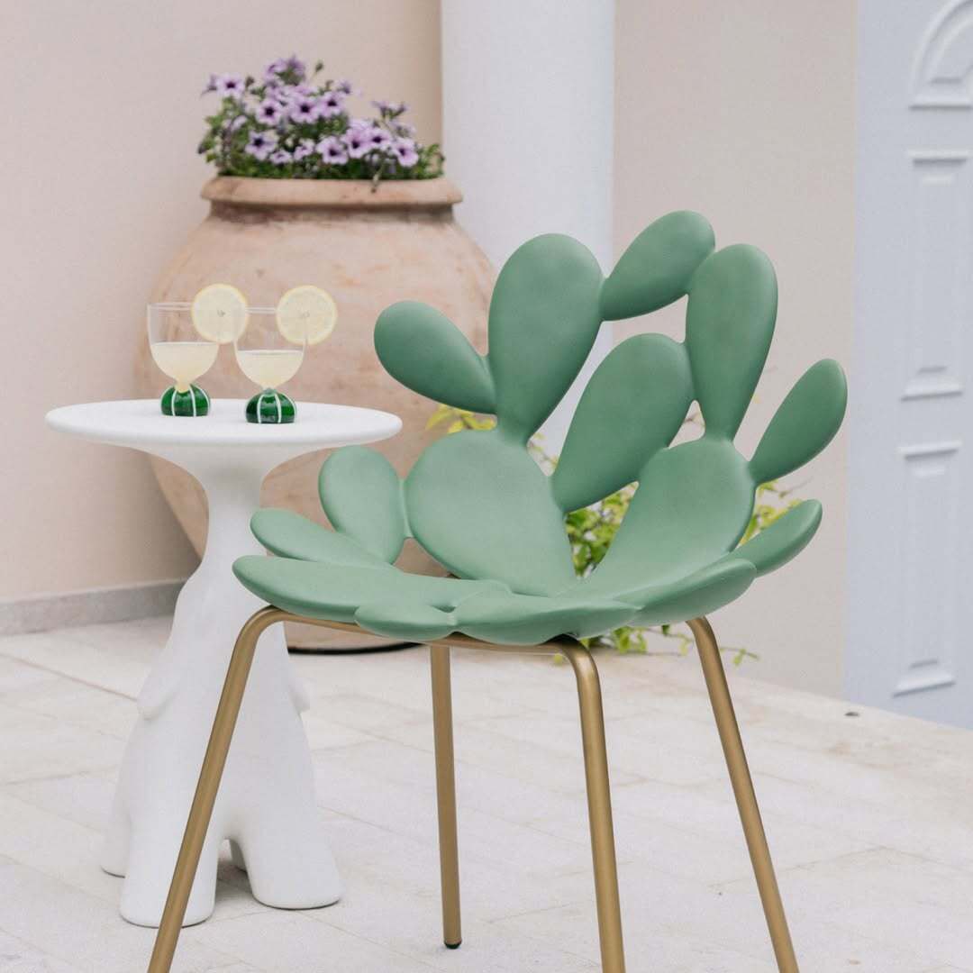 Filicudi chair by Marcantonio, green resin seat with gold legs, set outdoors beside white accent table.