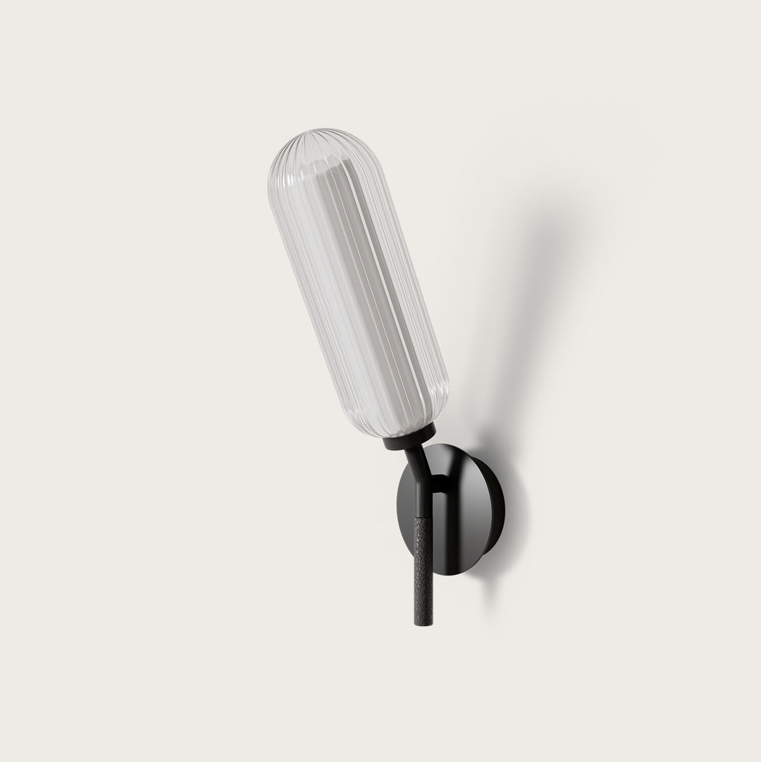 Lari Wall Lamp with fluted clear glass tube on a black arm and round wall plate, unlit, by Aromas del Campo