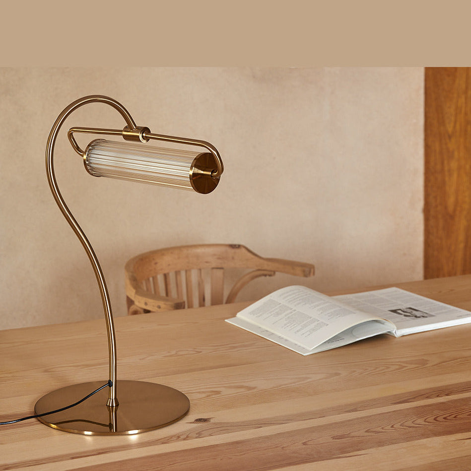 Ison Table Lamp in gold on a wooden table beside an open book and a bentwood chair