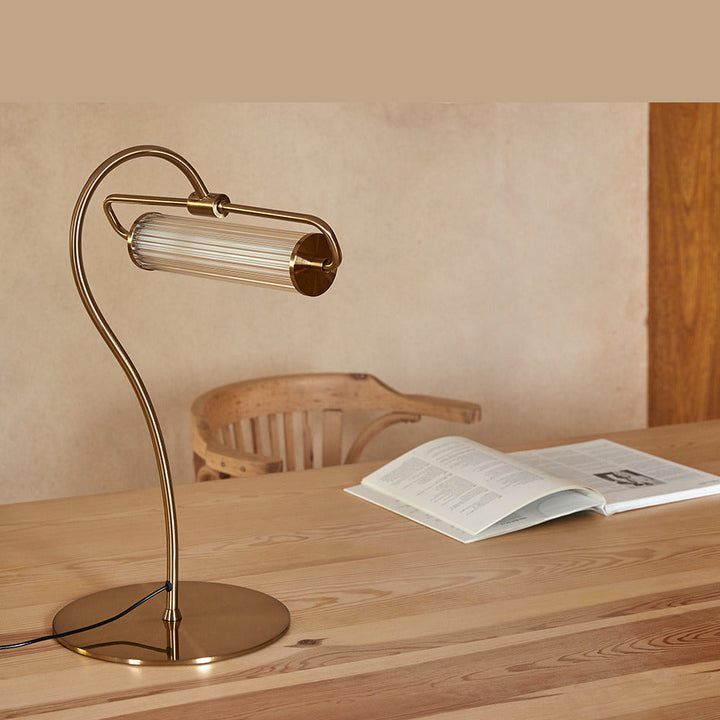 Ison Table Lamp in gold on a wooden table beside an open book and a bentwood chair