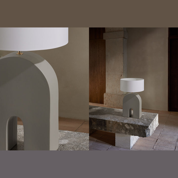 Home Table Lamp with a grey arched base and white shade on a rough stone bench in a rustic hall