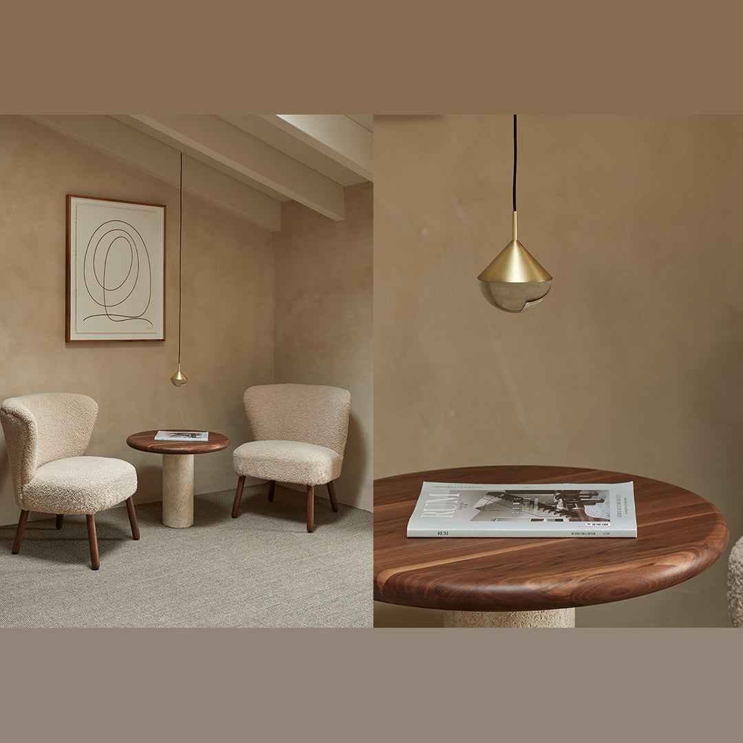 Brass Nino Pendant Lamp hanging over a round walnut side table between two boucle armchairs