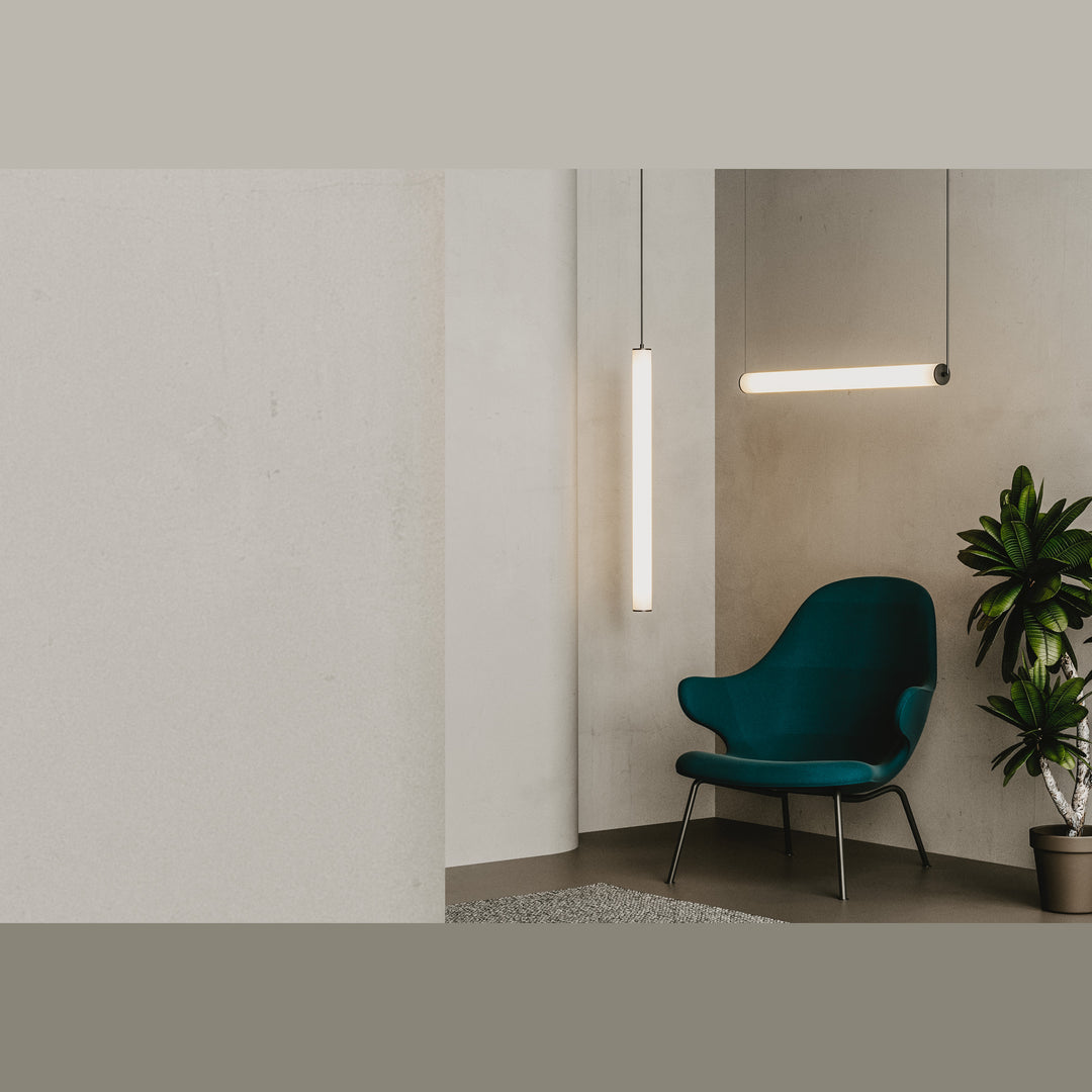 Tube Pendant Lamp lit, vertical and horizontal tubes above a green armchair and potted plant
